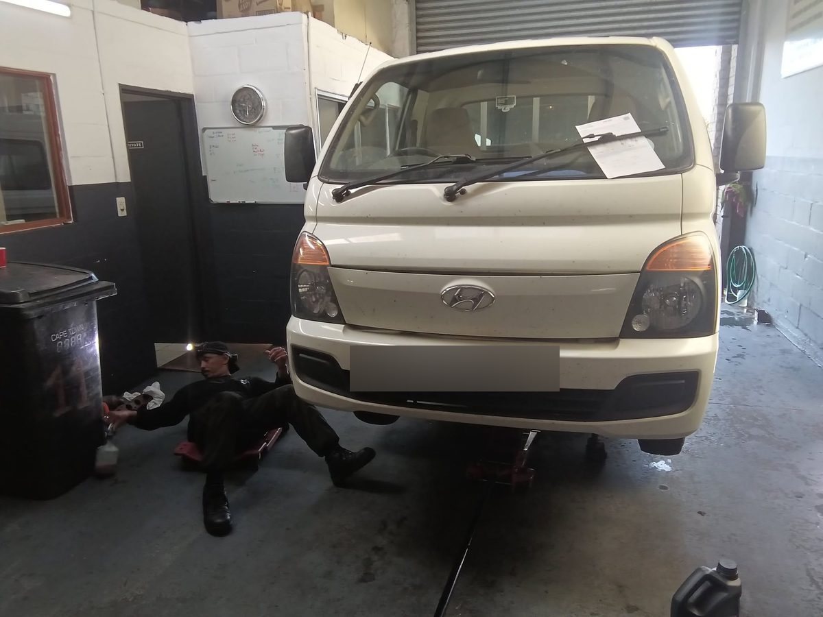 A technician working underneath a Hyundai H100 raised on a trolley jack.
